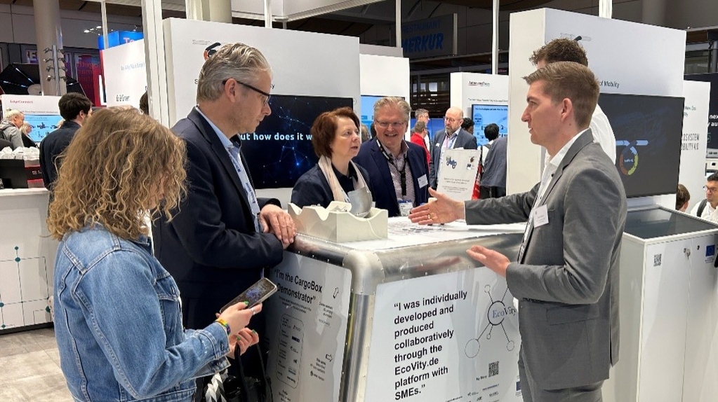 Teilnehmer diskutieren um einen Messe-Stand mit CargoBox-Demonstrator.