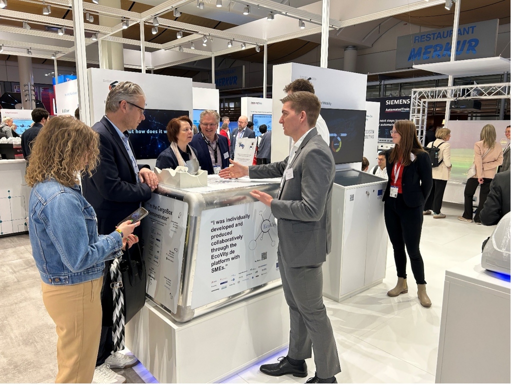 Teilnehmer diskutieren um einen Messe-Stand mit CargoBox-Demonstrator.