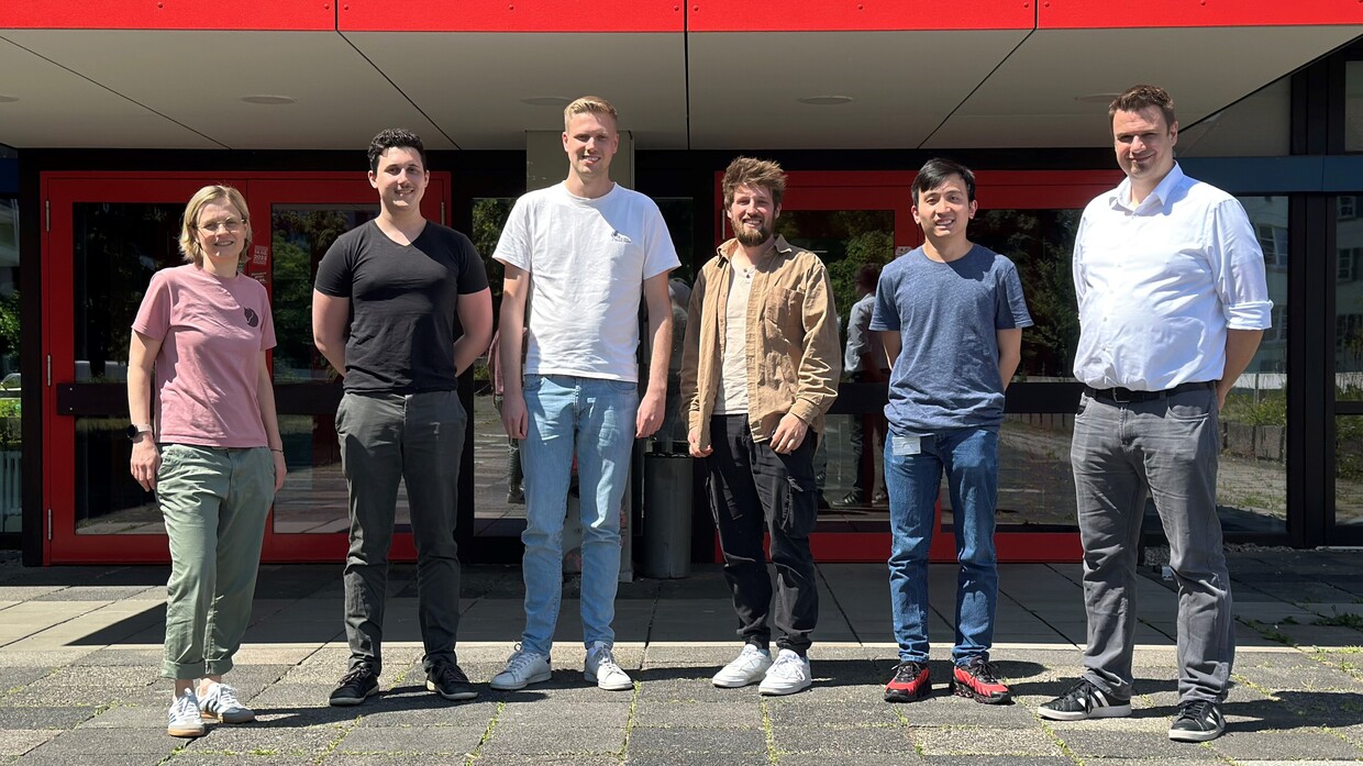 IMI Sechs Personen stehen vor einem Gebäude mit roten Türen und roten Paneelen.